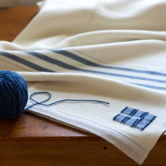 Swans Island's Grace Throw. 100% organic merino wool handwoven in Maine. Shown in white with Indigo.