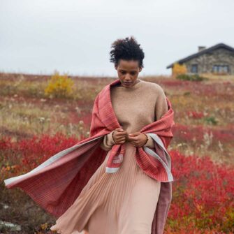 Model in a red blueberry barren, wrapped in Swans Island Katahdin Throw in Bittersweet. Soft merino wool, handwoven and hand-dyed with all natural dyes. Made in Maine.