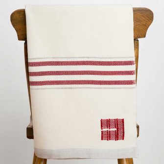 Swans Island Company's Grace Throw - a timeless classic. Handwoven in Maine with soft organic merino woo. Shown here in Natural with Winterberry Red stripe.