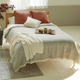 Swans Island Solid Winter blanket. Handwoven in Maine with locally sourced 100% Corriedale wool. Shown here in Dove on a bed with Bittersweet orange pillows.