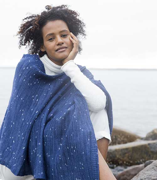 woman wrapped in shawl sitting on rocks by sea shore
