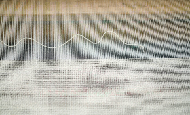 A single weft yarn wavers above a ground of plain weave creating a modern a graphic design on the loom at Swans Island Company.
