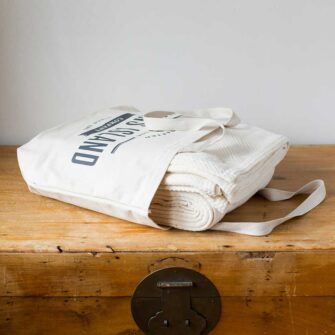 Swans Island Company's Charisma Blanket. Soft 100% Cotton blanket with woven herringbone texture. Made in USA with 100% American cotton. Shown here in Natural. Each blanket comes in a signature cotton tote.