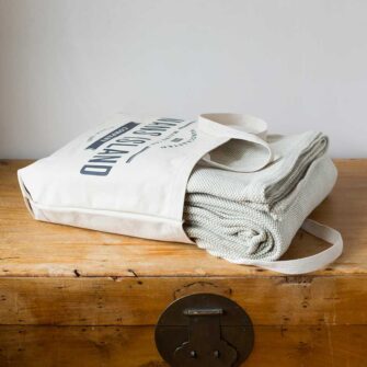 Swans Island Company's Savannah Blanket. Soft 100% Cotton blanket with woven herringbone texture. Made in USA with 100% American cotton. Shown here in Bayleaf. Each blanket comes in our signature cotton canvas tote.