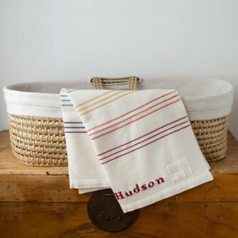 Swans Island Company's Rainbow Borders Baby Blanket. Handwoven in Maine with soft 100% organic merino wool. Comes in a signature linen box, perfect for gifting. Custom monogramming is available. Shown here with the name Hudson embroidered in Red.