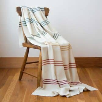 Swans Island Company's Rainbow Throw. All natural organic merino wool handwoven with band of 7 all-natural dyed stripes. Made in Maine. Shown in Natural with Brights.