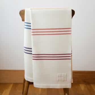 Swans Island Company's Rainbow Throw. All natural organic merino wool handwoven with band of 7 all-natural dyed stripes. Made in Maine. Shown in Natural with Brights.