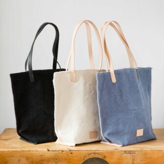 Swans Island Company's Hana Tote by Graf Lantz. Cotton Canvas with leather strap. Shown here in a trio of colors: Black, Natural, Horizon blue.