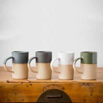 Swans Island Company's Tall Dipped Mugs are handcrafted with stoneware pottery dipped with a food-safe earthy glaze on top. Made in Maine. Shown here in Sage, Charcoal, White, Olive.