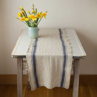 Swans Island Company's linen table runner by Linen Tales, made with 100% European Linen Oeko-Tex® and EUROPEN FLAX® certified. Made with stonewashed soft linen with mitered corners for a crisp edge. Shown here in Vintage Blue stripe on Flax with yellow daffodils on a white enamel table.