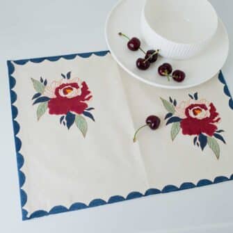 Swans Island Company's Babita Placemat by Soil to Studio. Block printed by hand in India with bright playful patterns. Shown here in Natural with Red rose floral and blue scalloped edge patterns..
