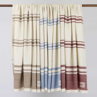 Casa Branca x Swans Island - Branca Stripe Grande Throw . 100% soft merino wool with hand-dyed stripes and ivory silk binding. Handwoven in Maine. Shown here in Biscotti, Winterberry, and Sky.