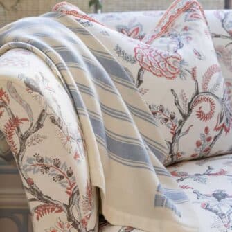 Casa Branca x Swans Island - Branca Stripe Throw . 100% soft merino wool with hand-dyed stripes and ivory silk binding. Handwoven in Maine. Shown here in Sky Blue draped on a toile patterned sofa.