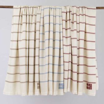Casa Branca x Swans Island - Branca Ticking Stripe Throw . 100% soft merino wool with hand-dyed stripes and ivory silk binding. Handwoven in Maine. Shown here in Biscotti, Winterberry, and Sky.